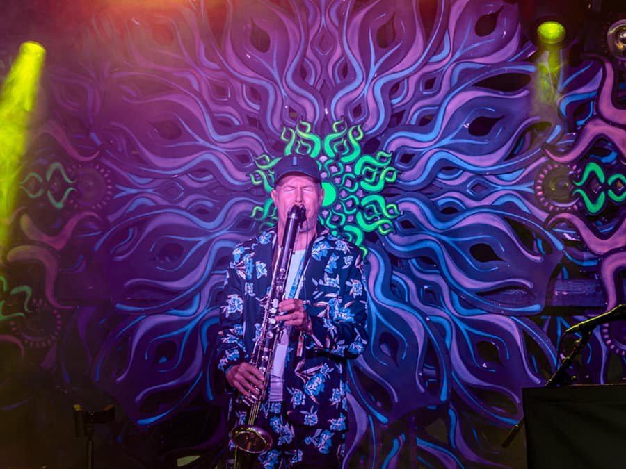 A RinneRadio saxophonist playing in front of a UV-lit psychedelic backdrop