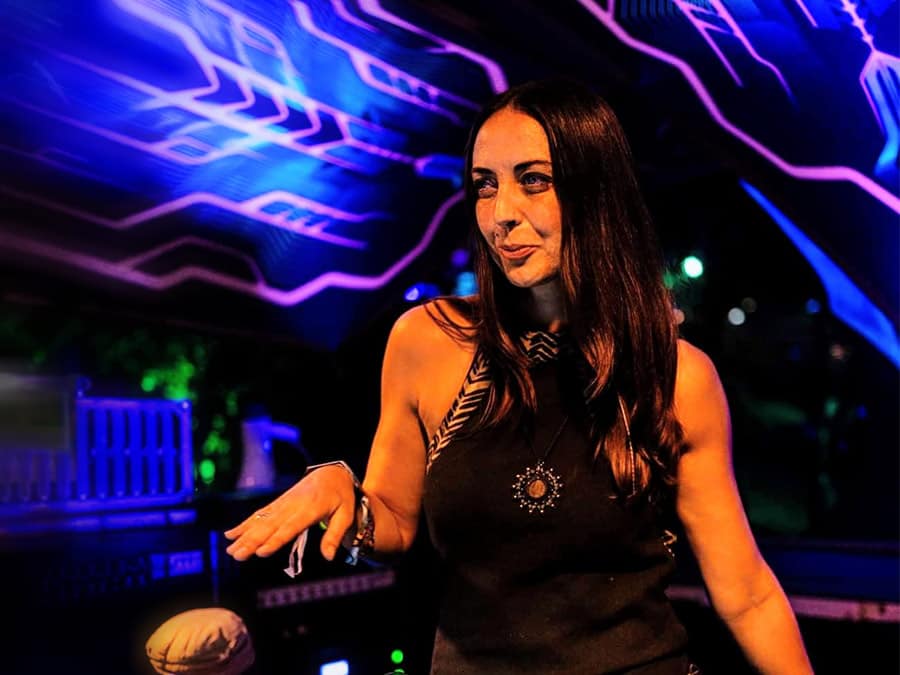 Naima smiling at the decks in front of a blue-lit stage