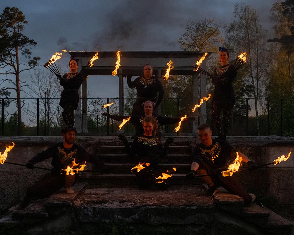 The Roihu group posing with fire props on outdoor steps at dusk