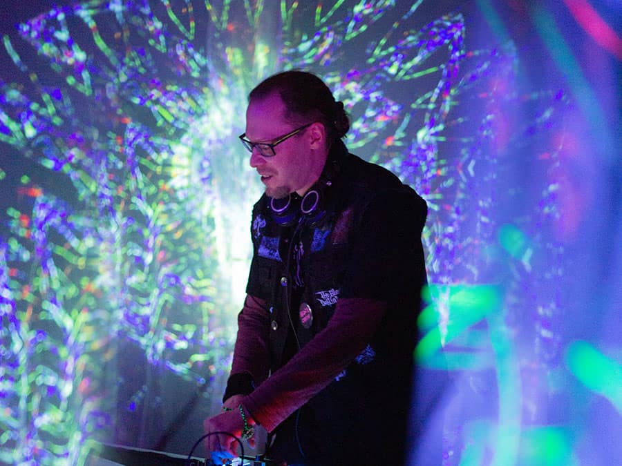 Deidriim in glasses and headphones DJing in front of projected light patterns