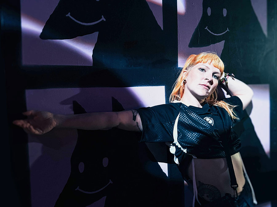 Mary Young with orange hair dancing in front of projected smiley faces