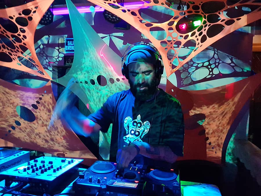 Uaky DJing in headphones under UV-lit string art