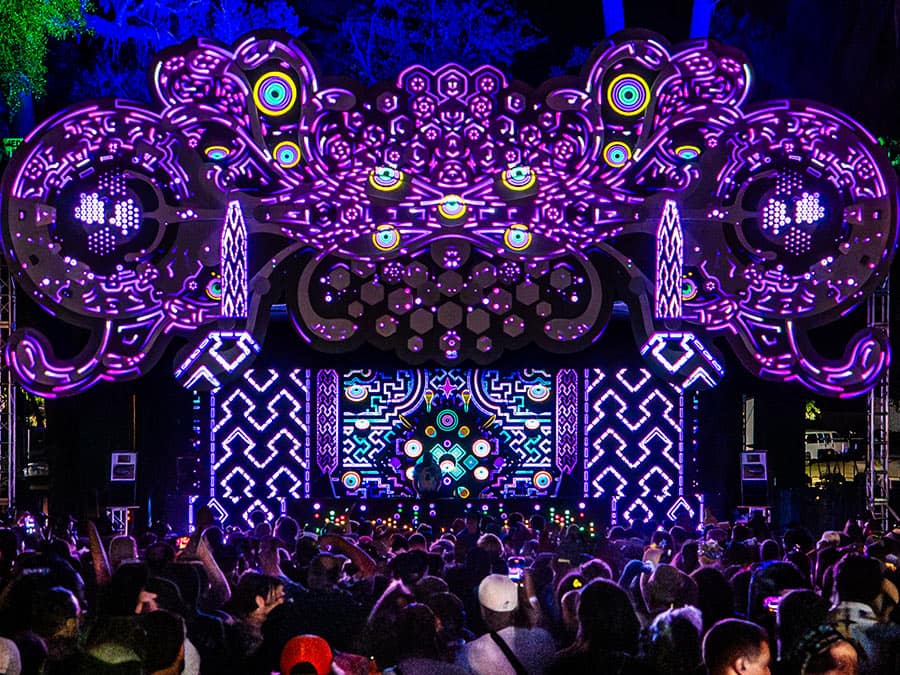A crowd in front of a huge UV-lit psychedelic stage installation
