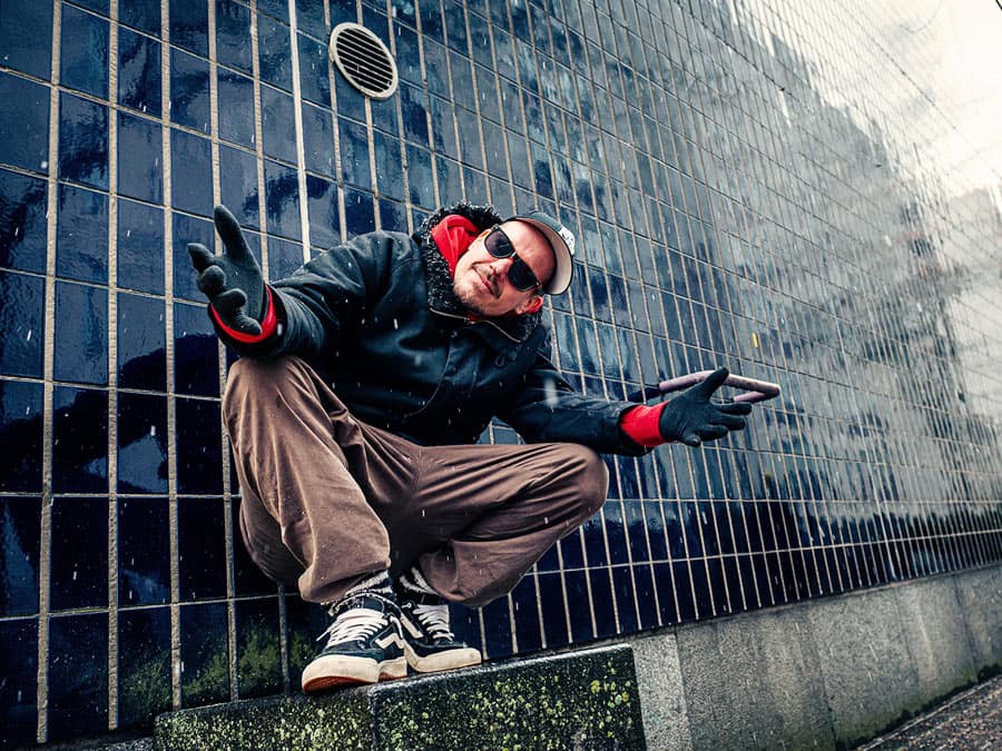 Laineen Kasperi in sunglasses and a red cap, crouching on a ledge and gesturing at the camera