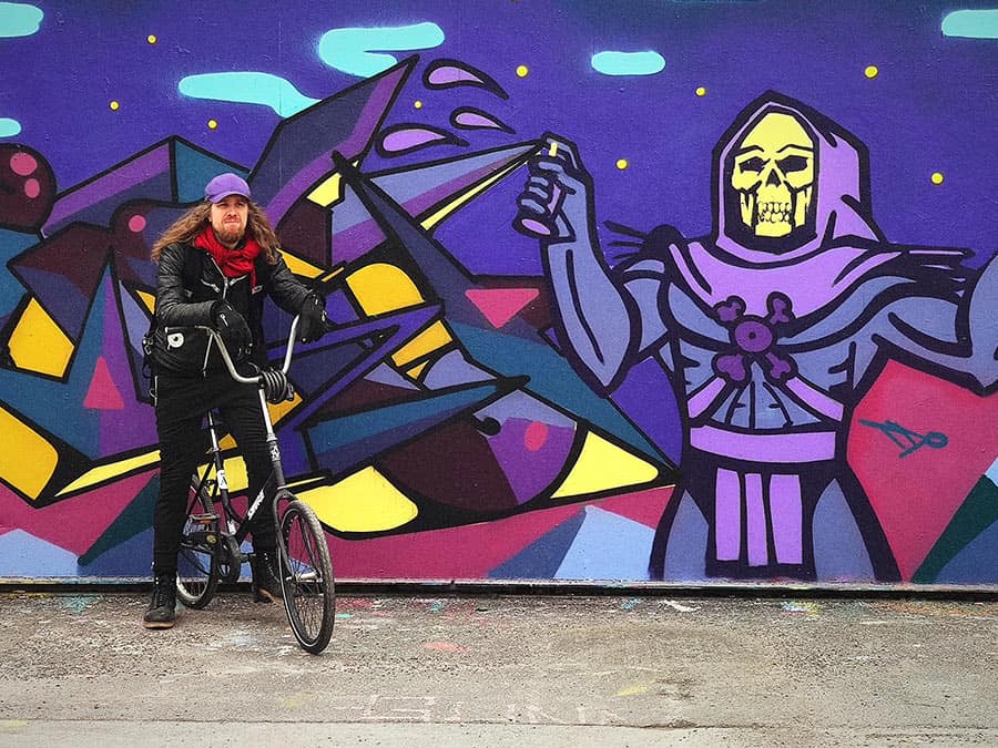Vishnudata with a bicycle in front of a colourful graffiti mural