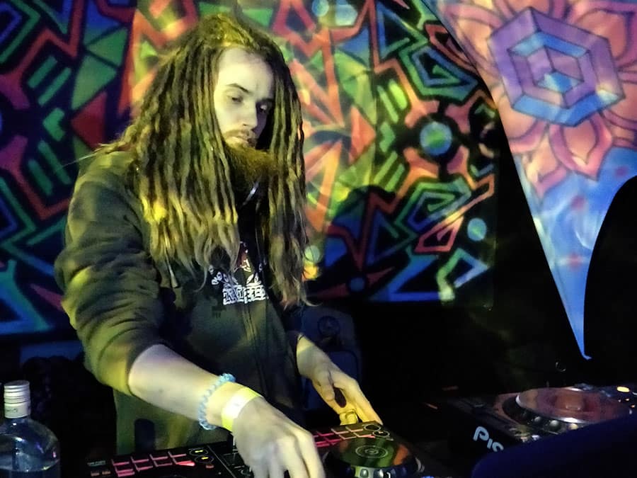 Cosmic Touch with long dreadlocks playing at the decks in front of UV decor