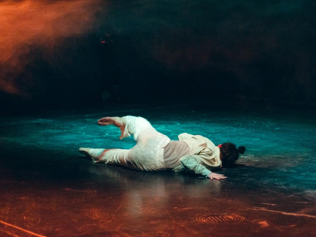 Silve lying on a stage floor in white clothes under teal light