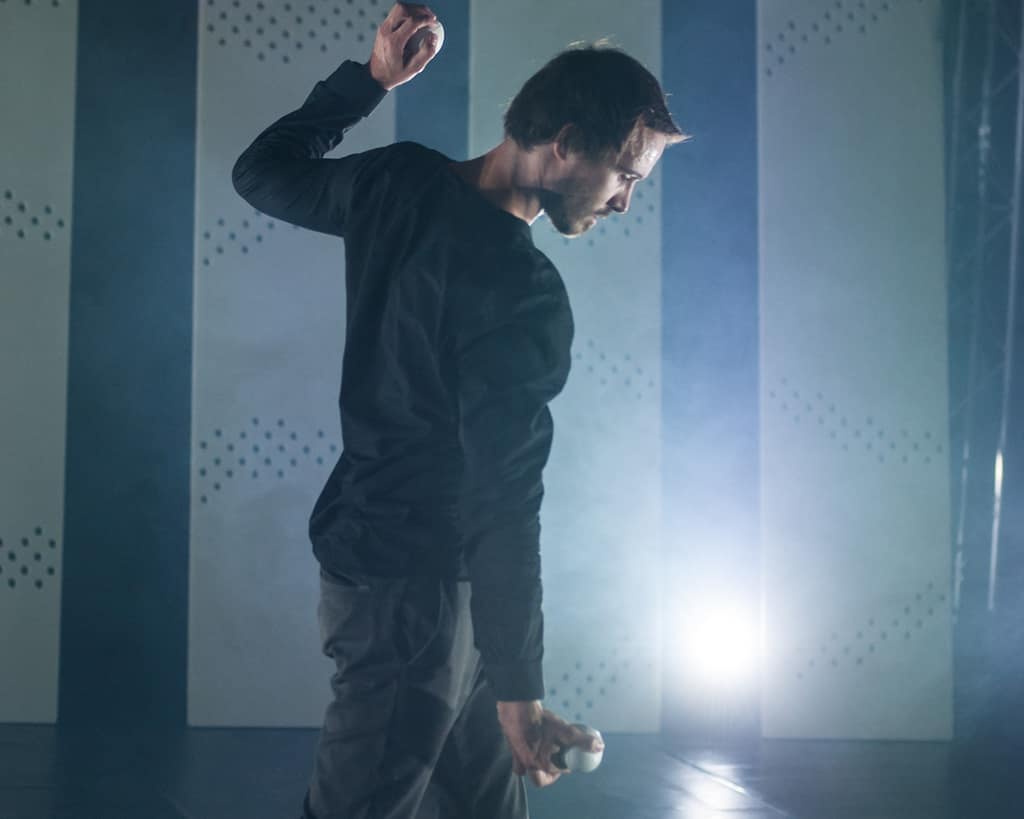 A performer in black mid-movement in a smoky, backlit room