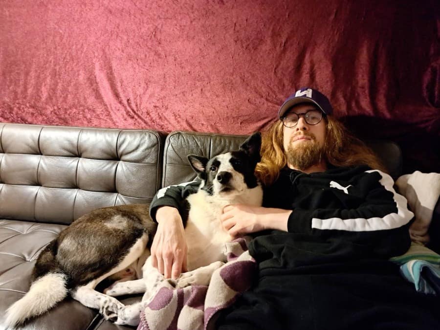 Valo Elios in a cap and glasses relaxing on a leather sofa with a dog