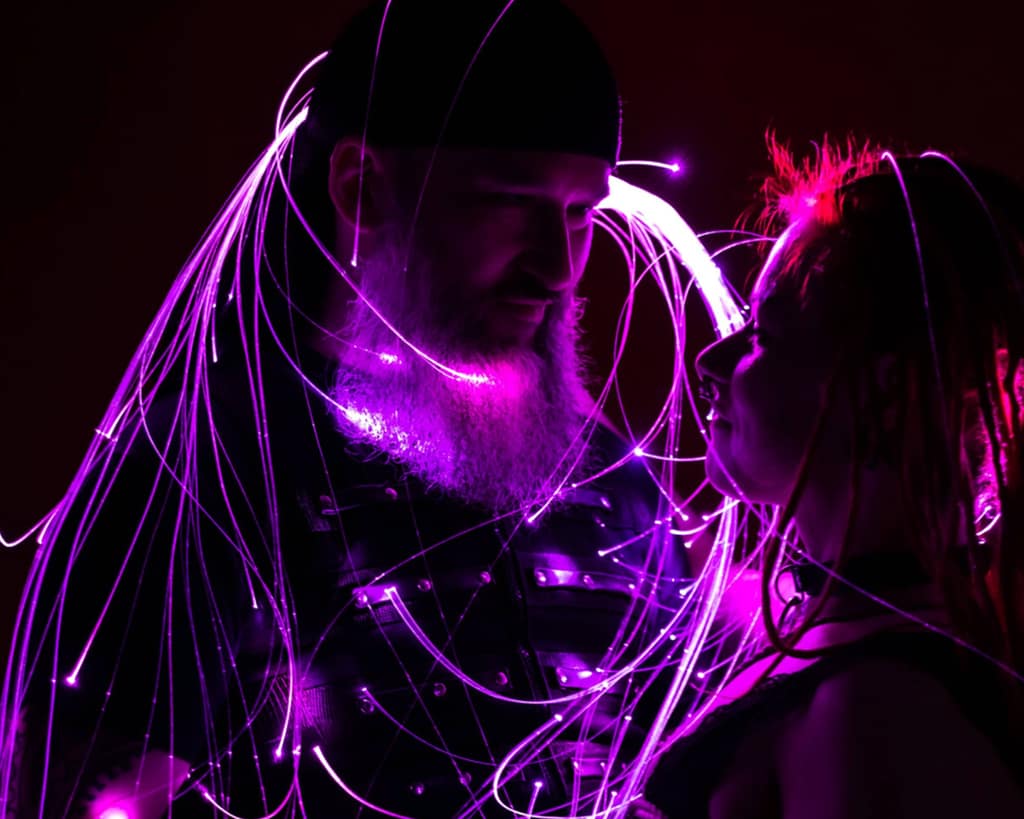 Two people wrapped in glowing purple strands of fibre-optic light
