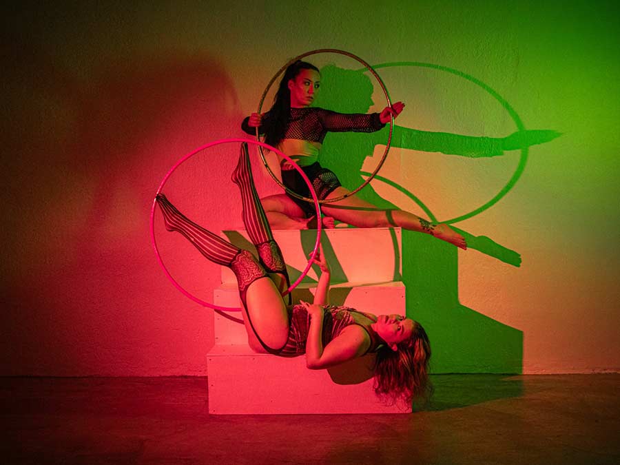 The TwinBlaze duo in an acrobatic pose with hula hoops against red and green light