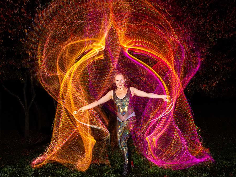 A performer surrounded by long-exposure trails of orange and pink LED light