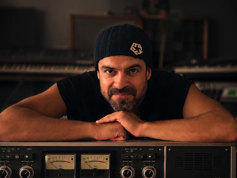 CYEAD in a beanie, leaning on an analogue mixing desk in a studio