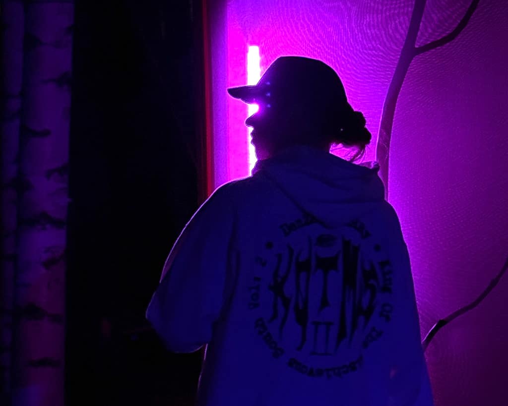 kaju in silhouette wearing a hat against a magenta light