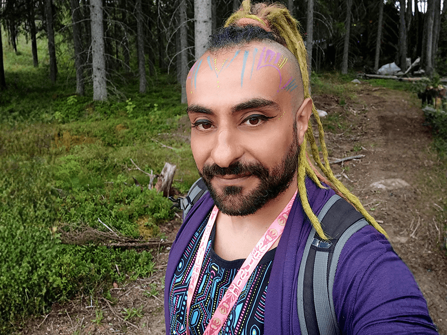 Liquid Ahmed with long braids smiling in a forest selfie
