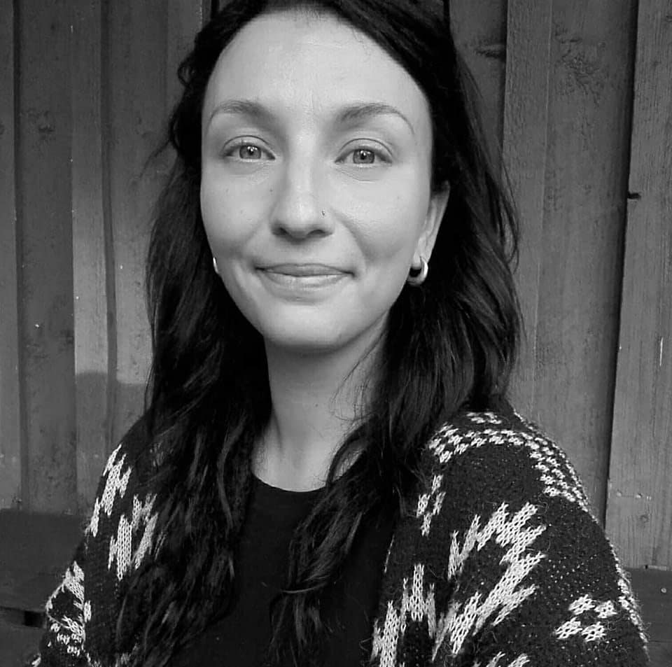 Black-and-white portrait of Saara-Elina, smiling, with long dark hair and a patterned cardigan