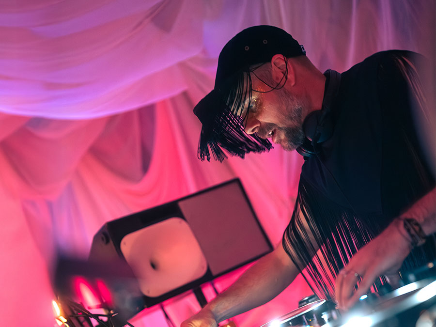Herra Huu in a cap playing a DJ set under pink light