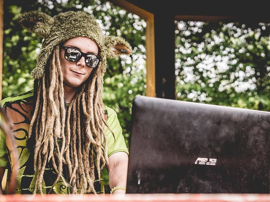 Tigro with long dreadlocks, sunglasses and a furry hat behind a laptop