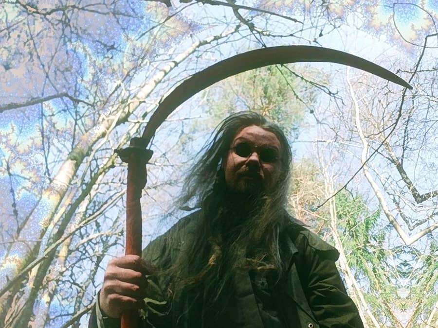Kalma with long hair holding a scythe among trees