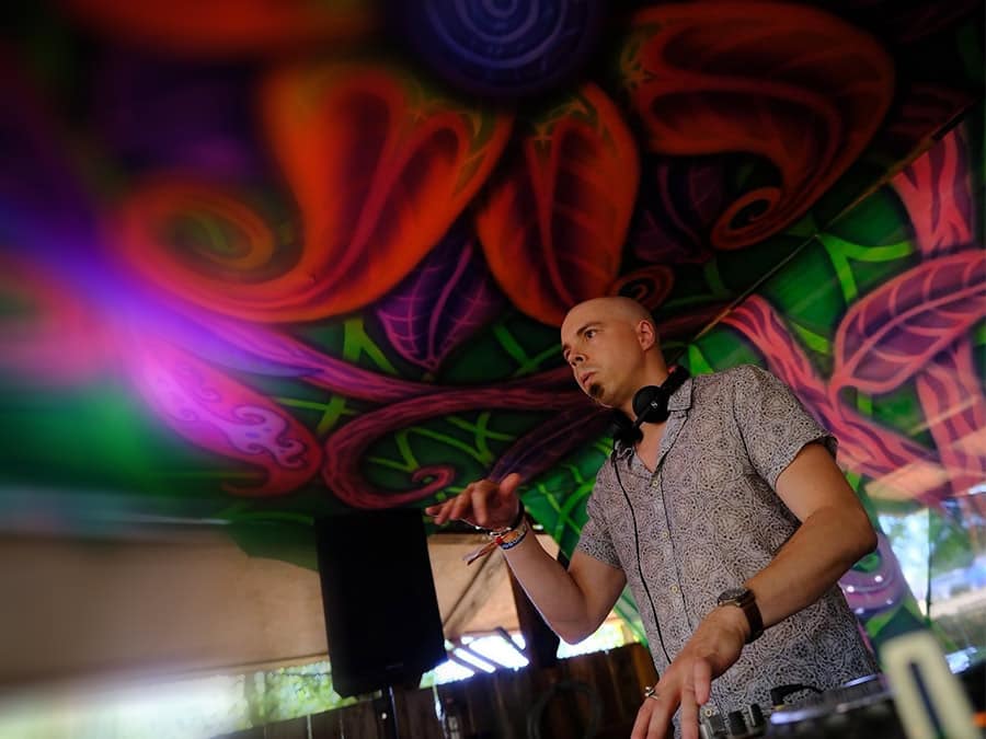 Nebula Meltdown in headphones at the decks under a psychedelic canopy