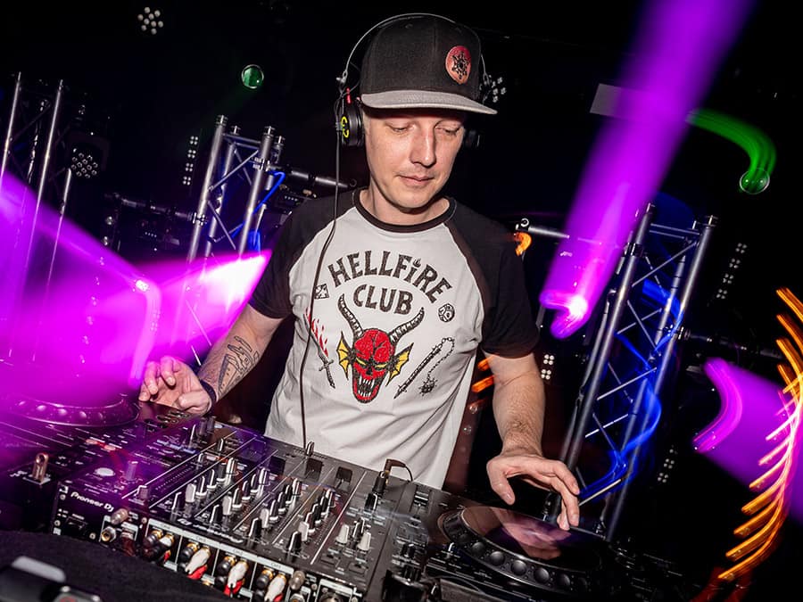 Alchemiist in a cap and headphones at the decks with pink stage lights