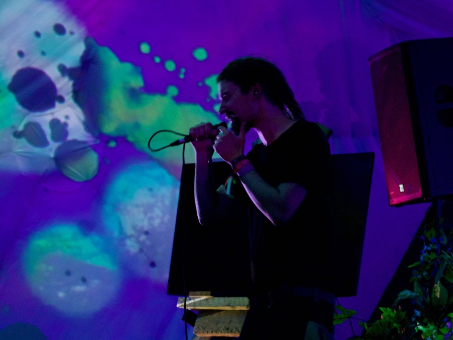 Iki rapping into a microphone in front of UV-lit projections