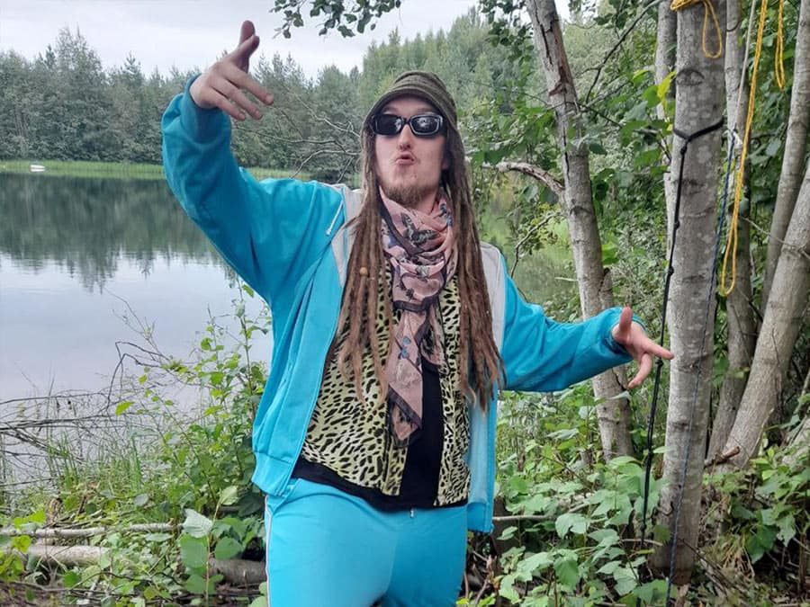 Lurjus in a turquoise tracksuit and sunglasses, posing by a lake