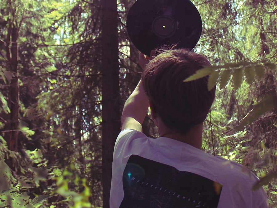 Mysteerisignaali in a forest holding a vinyl record up in front of his face