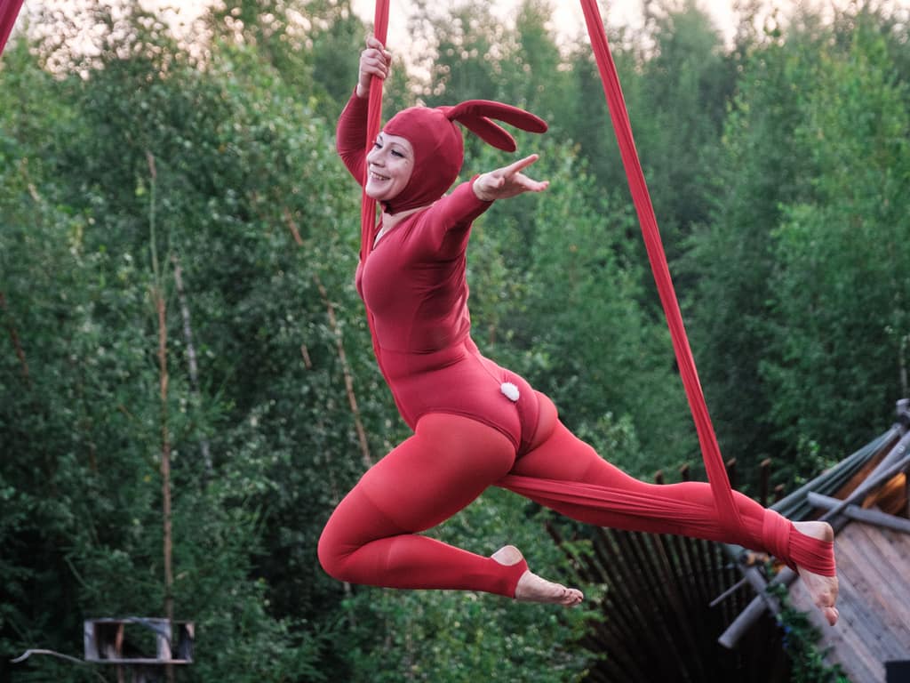 DancingMonaLisa in a red bunny costume performing on a red aerial hammock in a forest