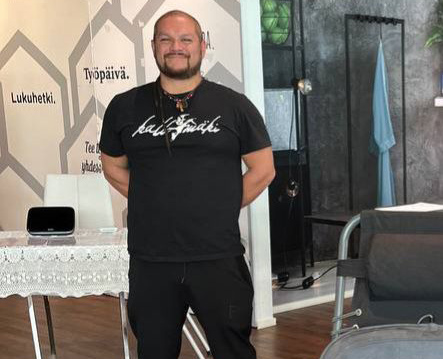 Duvan, a smiling bearded man in a black T-shirt, standing in a treatment room