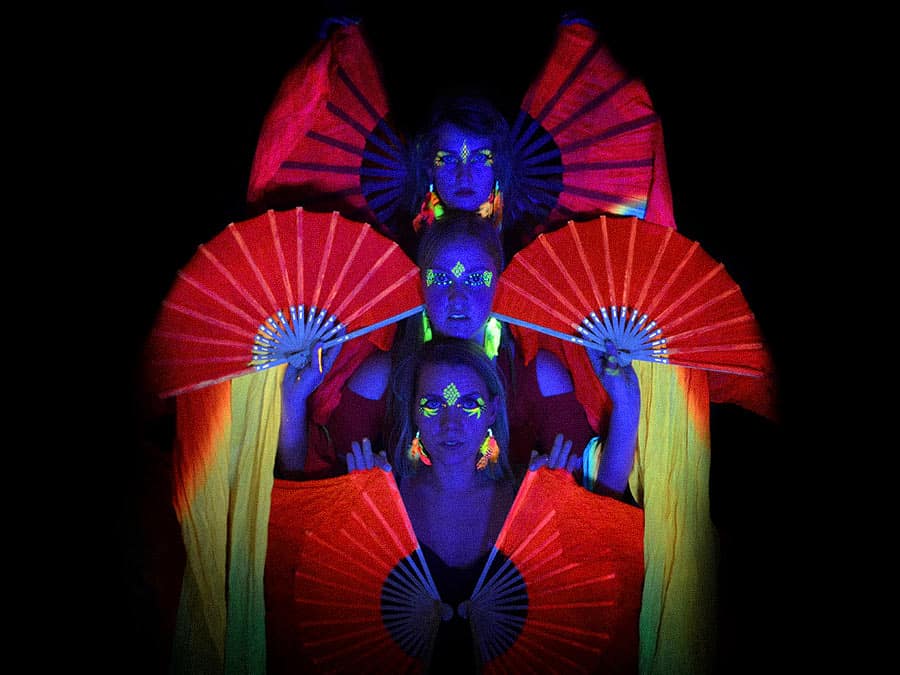 Three Viuhkea dancers with UV-painted faces framed by red silk fans