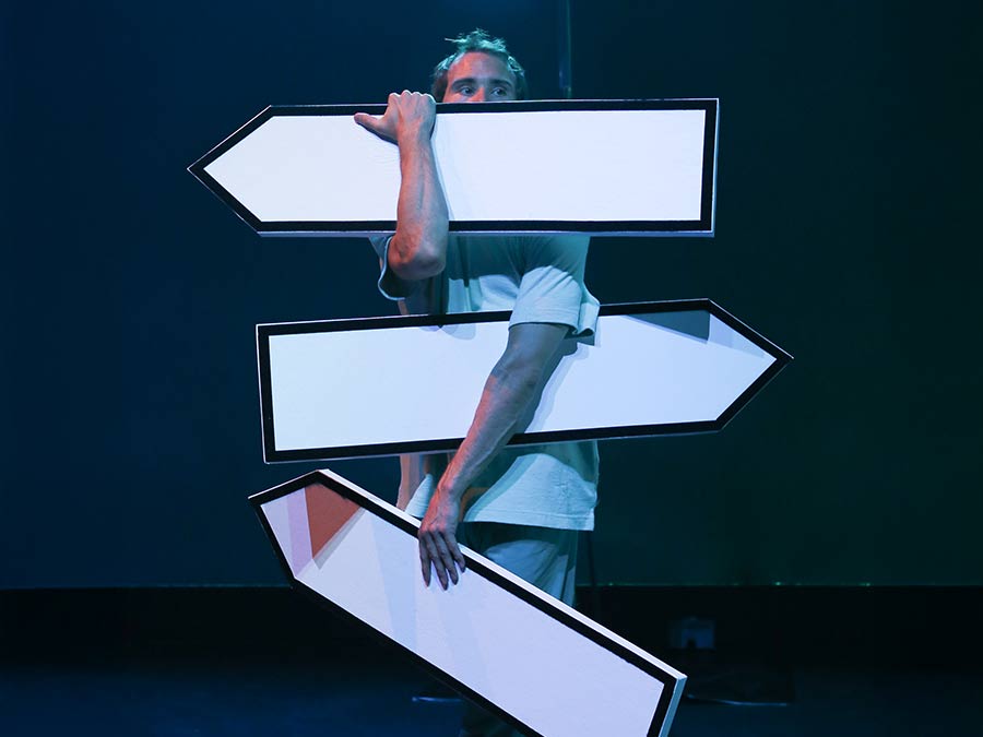 Olli Vuorinen on stage holding three road signposts pointing in different directions