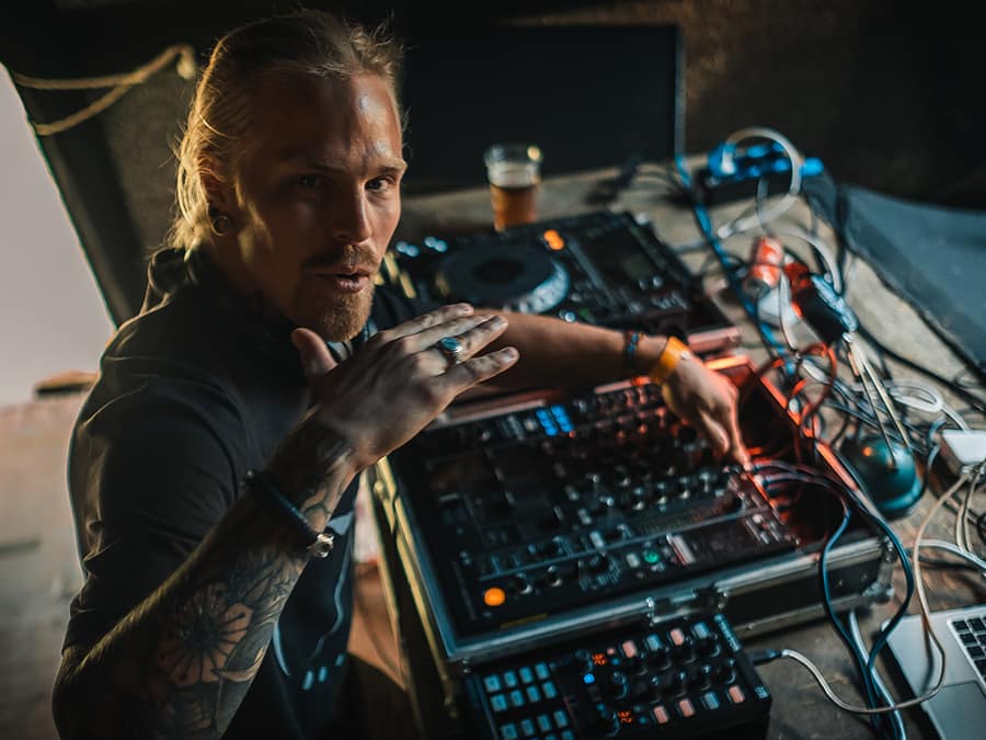 Yonagual at a table of electronic music gear, looking into the camera