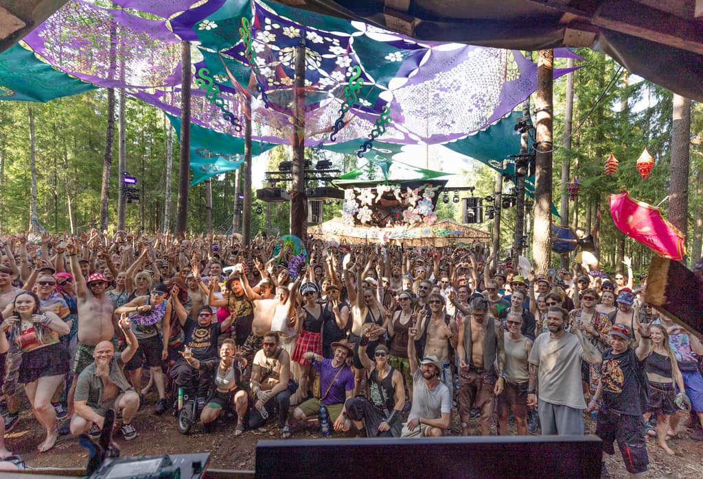 A crowd raising their hands under the colourful canopy of a forest stage at Kosmos Festival 2026