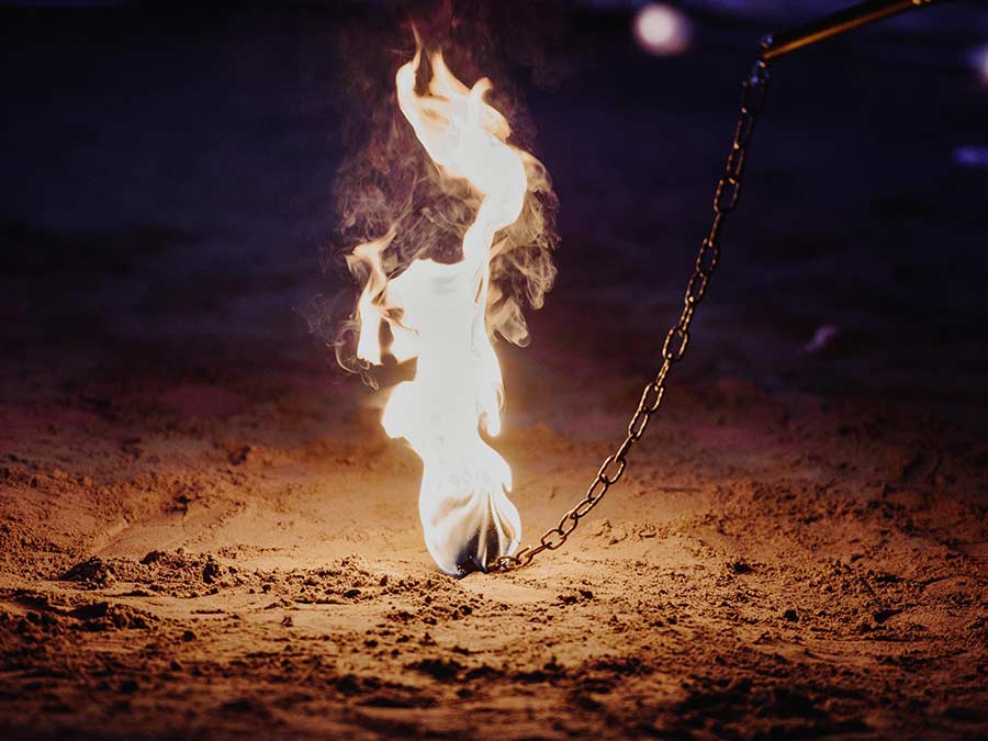 A burning rope dart on its chain above the sand
