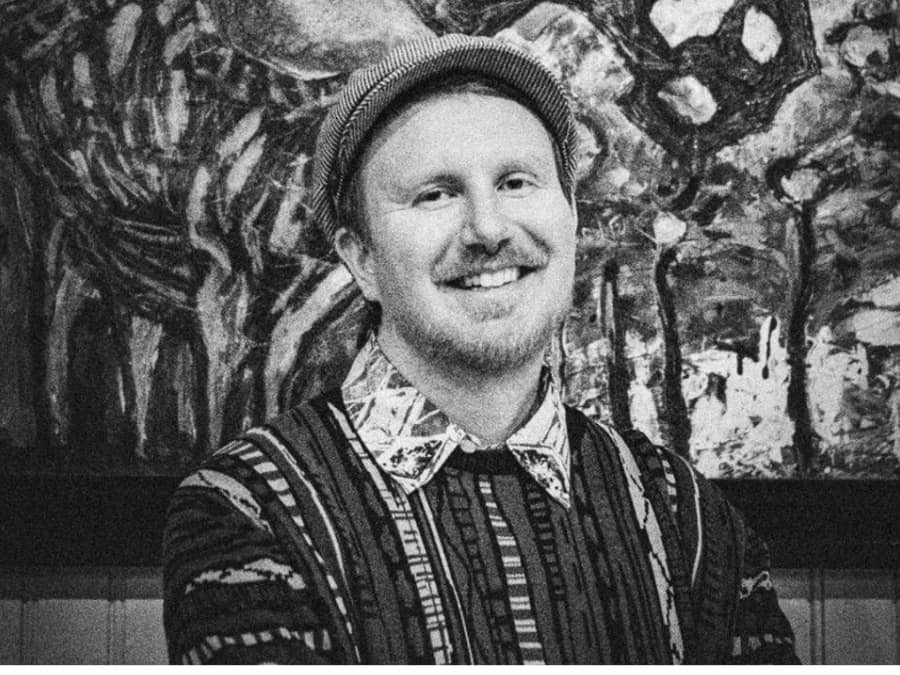 Black-and-white portrait of a smiling Rongoā in a knit cap and patterned sweater