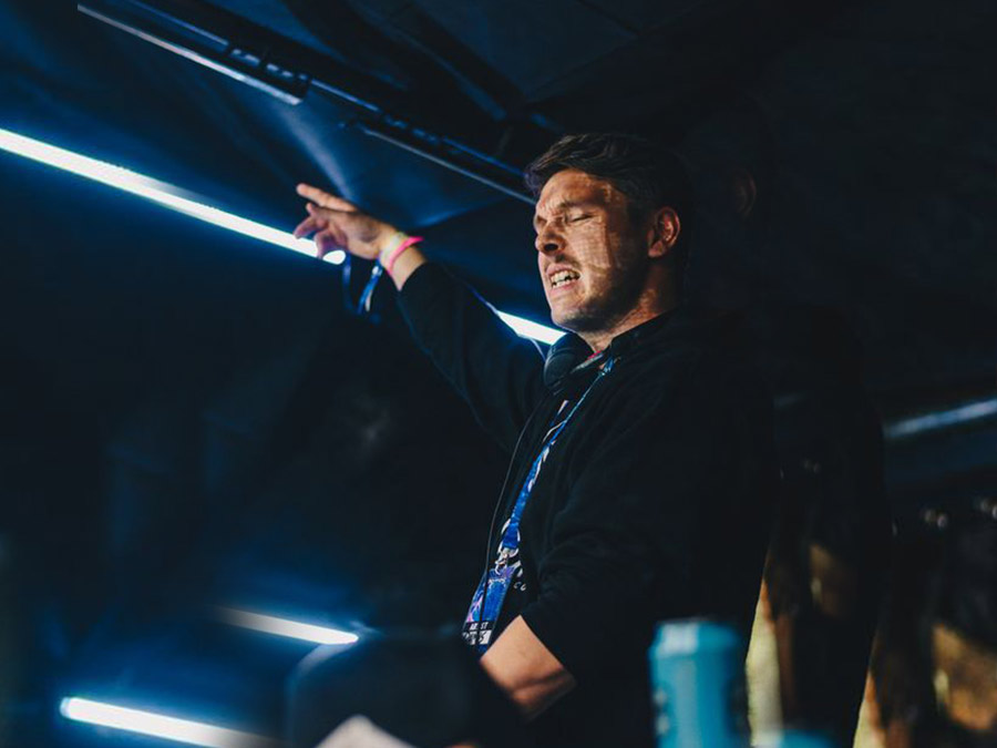 Damus pointing to the crowd from the DJ booth in blue light