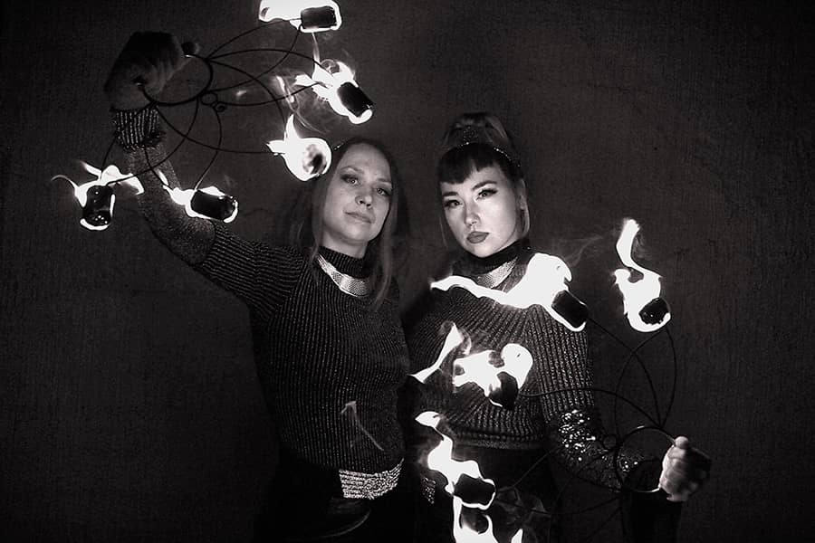 Black-and-white photo of FlowingLinda and Miralkemia holding flaming fans