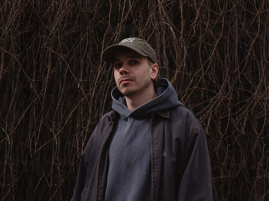 Jeku in a cap and hoodie in front of bare branches