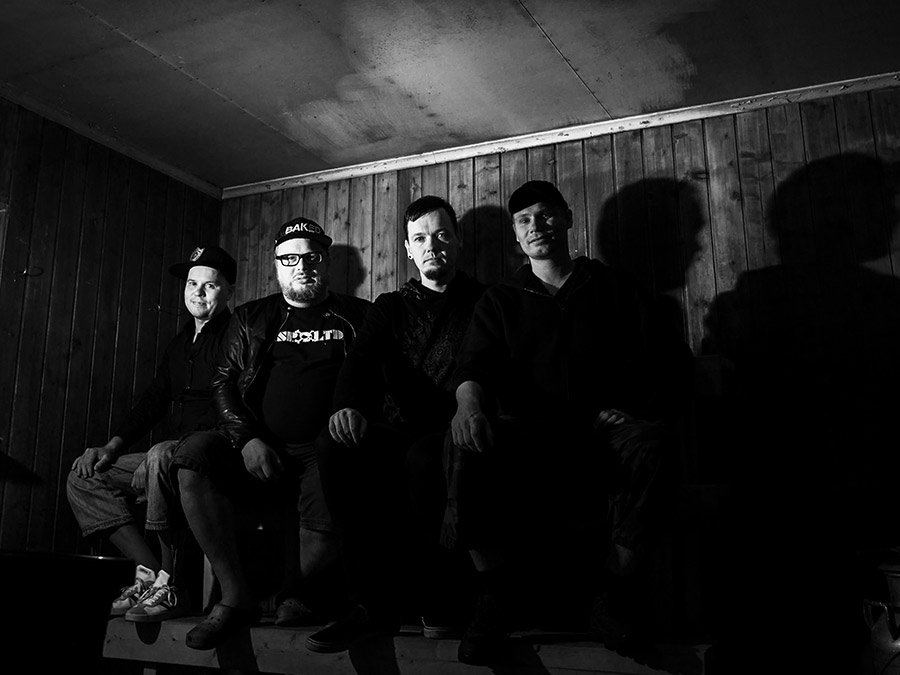 Black-and-white group photo of the four members of Carbon Based in a wooden room