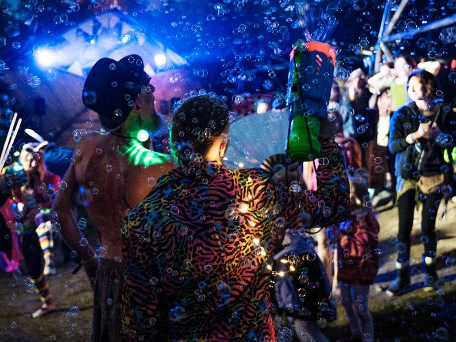 Costumed festival-goers surrounded by soap bubbles at night