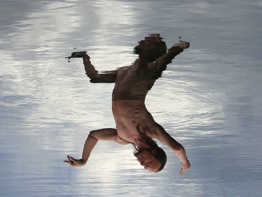 An upside-down image of a butoh performer with outstretched arms against pale water