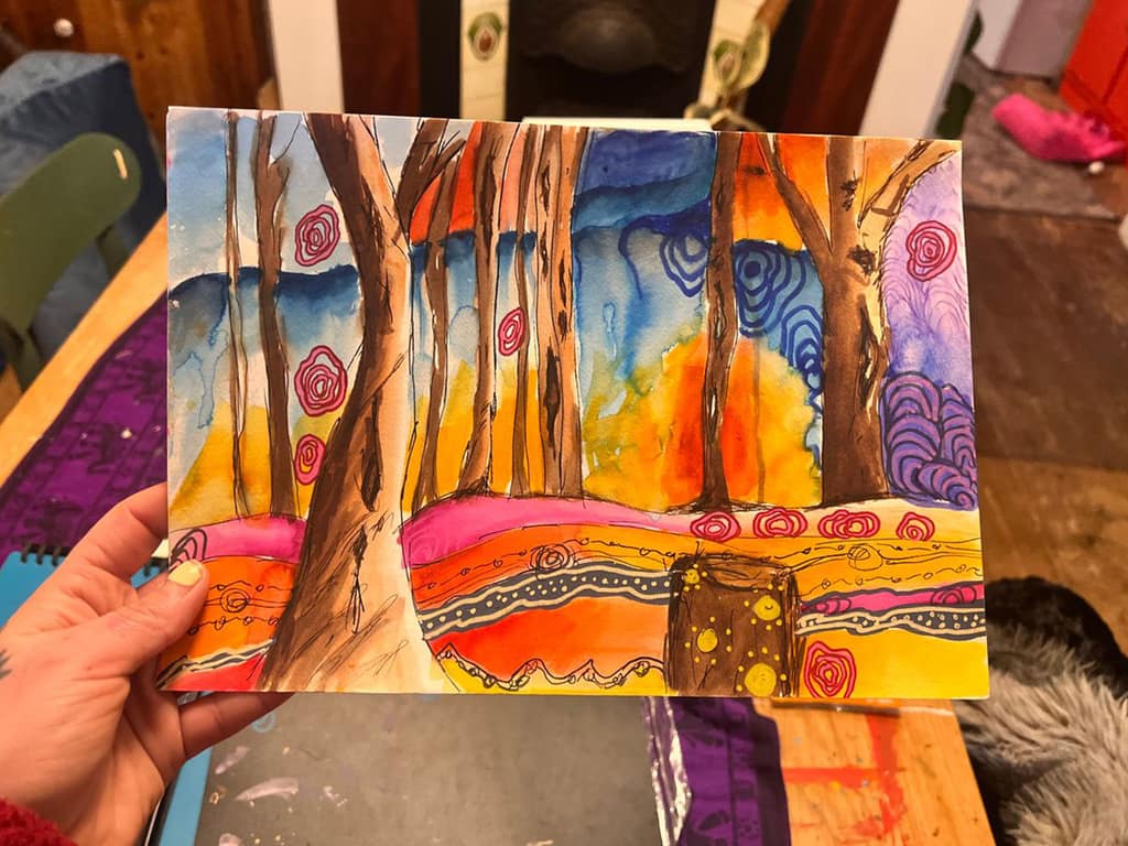 A hand holding a watercolour painting by Warluyinya of tree trunks against bright orange, pink and blue patterned bands