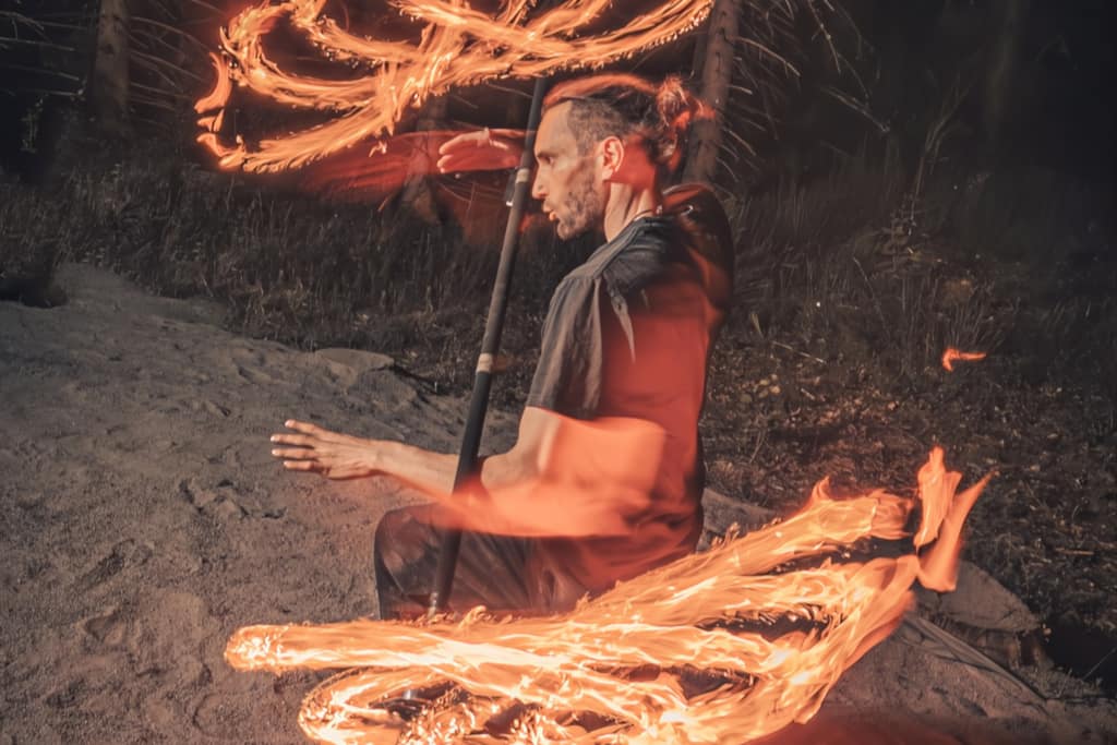 Azuh spinning fire props that leave glowing trails on a sandy shore